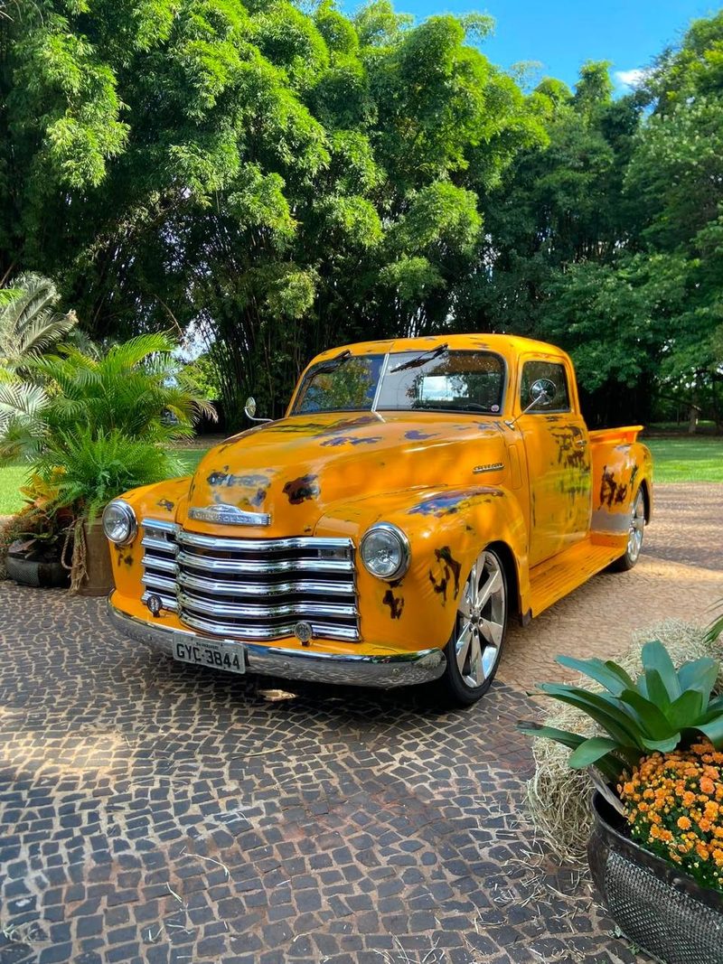 Picape Chevrolet 3100 Boca de Sapo 1950 amarela com pintura envelhecida, montada em um jardim para evento